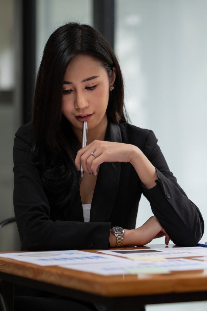Confident young woman calculating expenses on a laptop while reviewing financial documents.