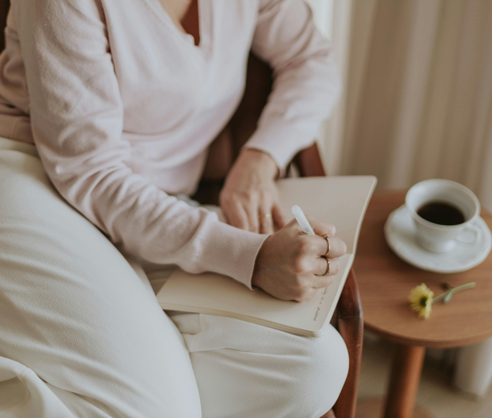 Woman journaling at a desk after her morning routine, illustrating habit stacking and building positive daily habits.