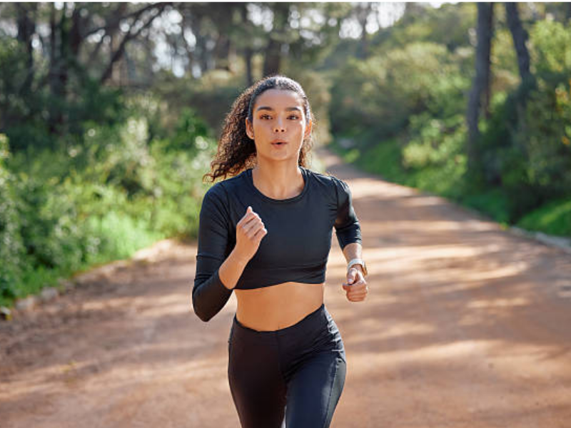 A woman running outdoors, focused and energetic, engaging in physical exercise for fitness and well-being.
