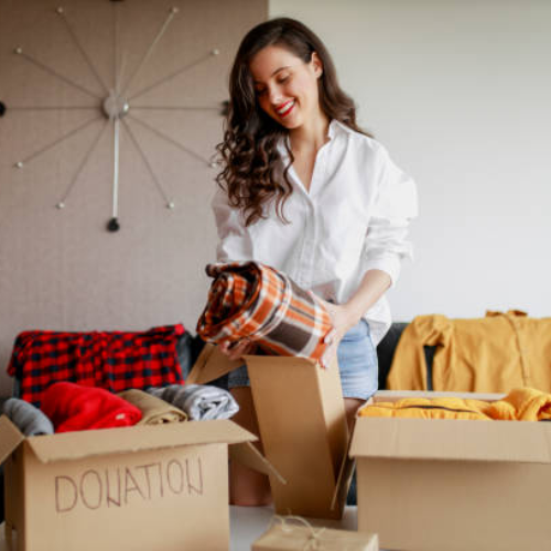 Woman placing folded clothes into donation boxes during home decluttering and wardrobe clean-out.