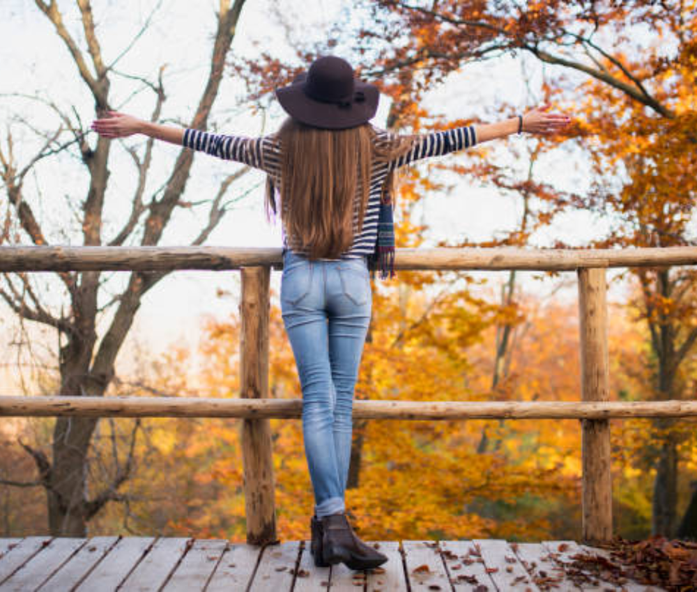 female that is fashionable dressed for fall and looking at the beautiful fall leaves.