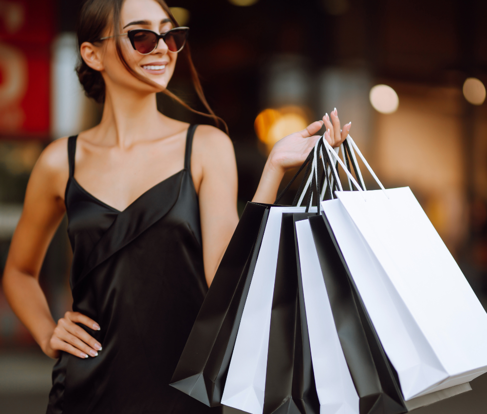 Smiling woman standing in front of an organized capsule wardrobe with neatly arranged clothing and accessories for effortless mornings.