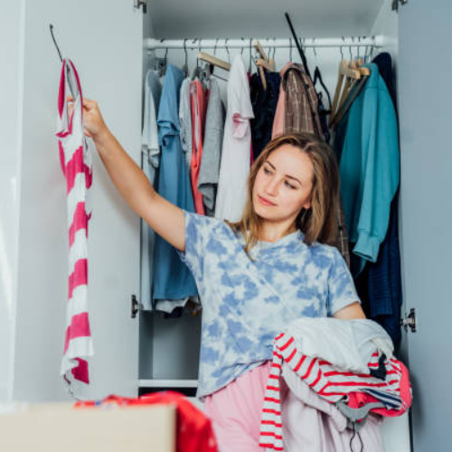 Woman cleaning out bedroom closet, sorting clothes into keep, donate, and discard piles for decluttering and organization.