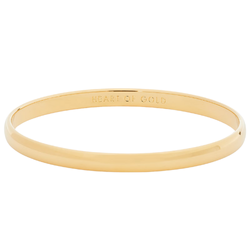 Kate Spade Heart of Gold Idiom Bangle in gold-tone metal with engraved detailing, displayed on a clean surface, highlighting its elegant and stylish design as a statement jewelry piece.