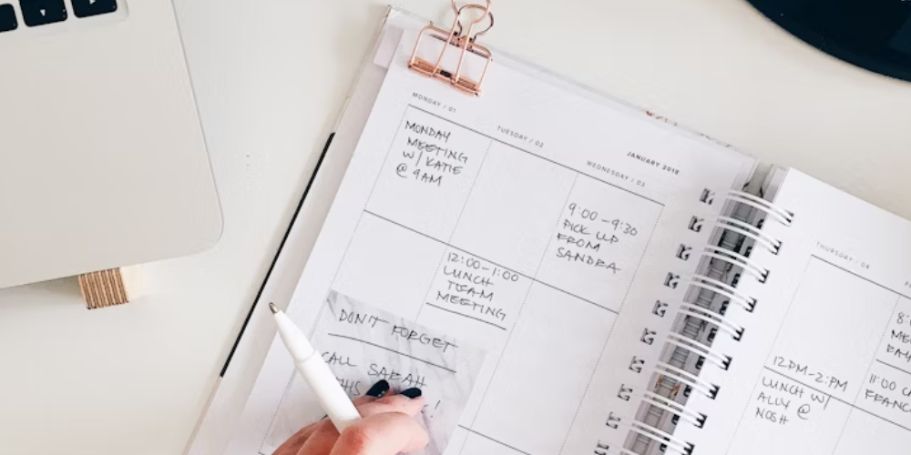 A woman writing in a planner at a desk, organizing her schedule and planning her day for better productivity.