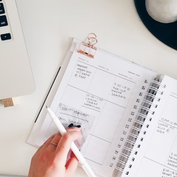 A woman writing in a planner at a desk, organizing her schedule and planning her day for better productivity.