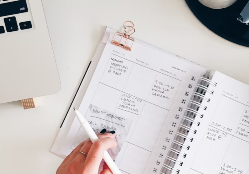 A woman writing in a planner at a desk, organizing her schedule and planning her day for better productivity.