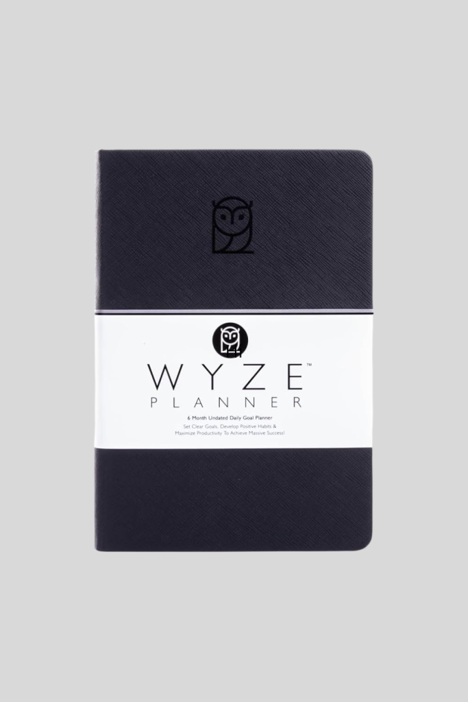 Wyze Planner open on a desk, displaying daily, weekly, and monthly layouts for goal-setting, task management, and habit tracking.