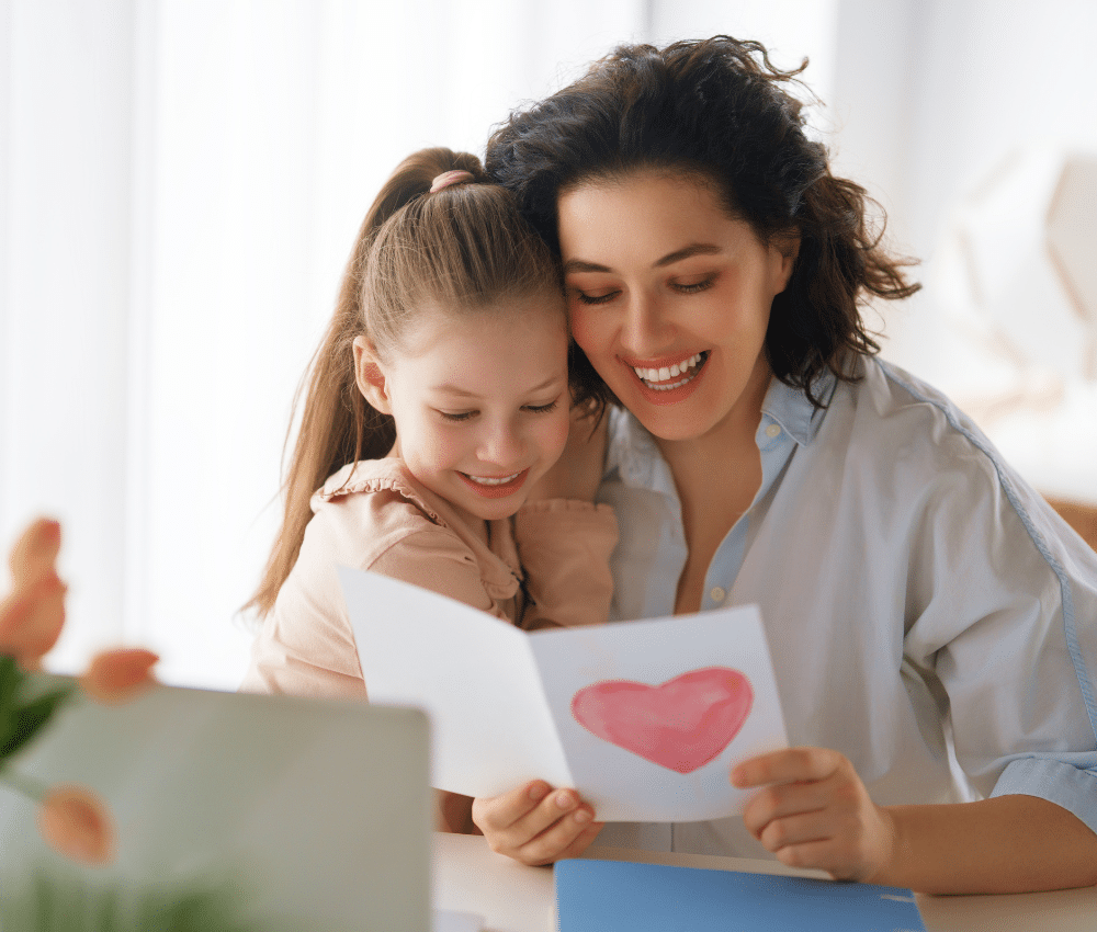 Mother and daughter embracing and looking at a card made by the daughter.